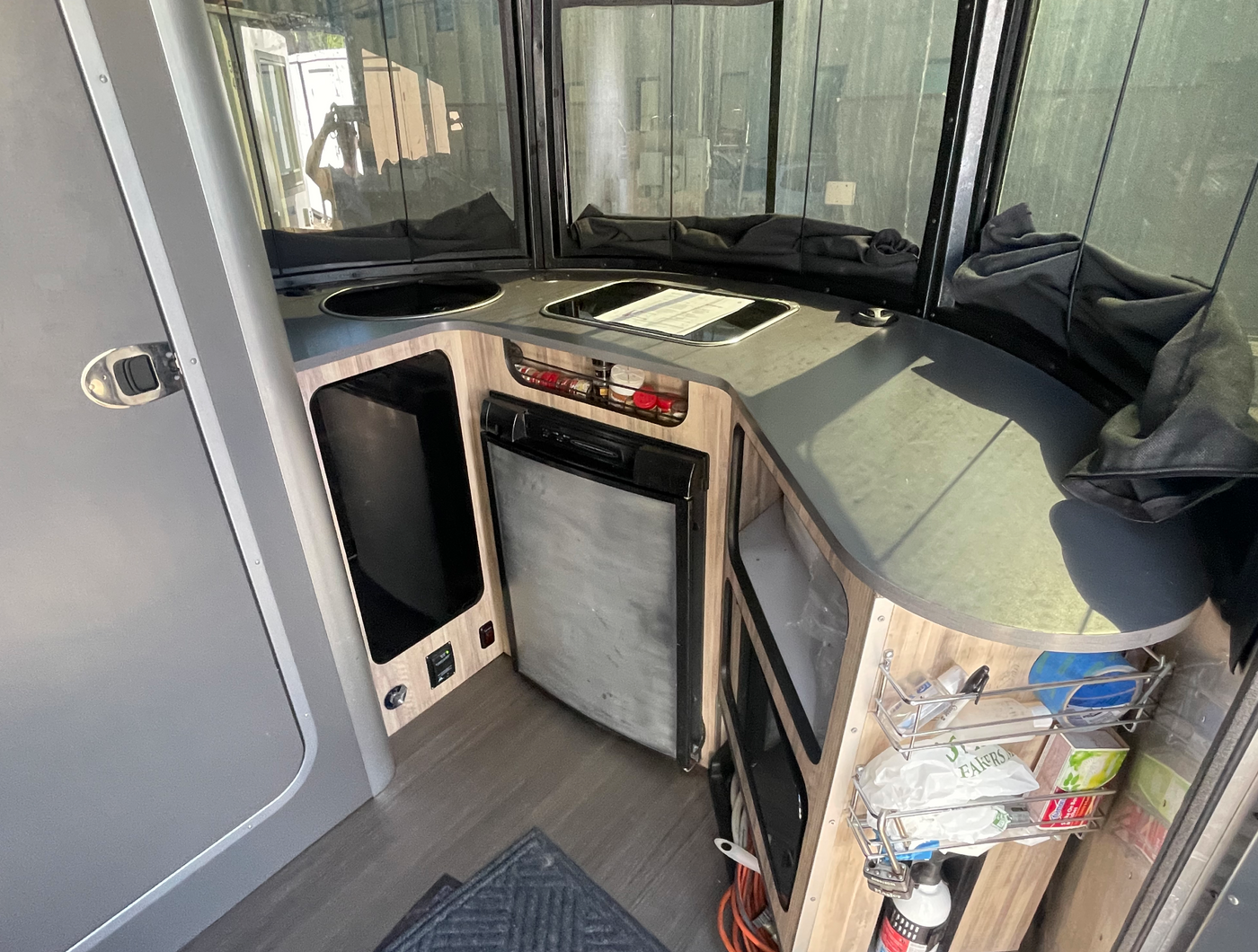 This RV rental kitchen includes a sink, stovetop, and fridge, with wood-grain cabinets and dark countertops, perfect for road trip cooking. — photo 4
