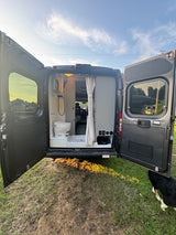 Rear view of an RV rental camper van with open doors, showcasing its integrated bathroom with a toilet and shower.