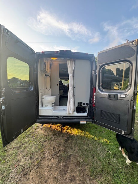 Rear view of an RV rental camper van with open doors, showcasing its integrated bathroom with a toilet and shower.