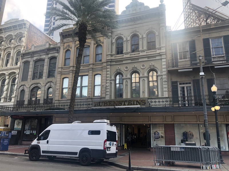 A white RV rental van parked outside Rubenstein's historic store in New Orleans, amidst grand old buildings and a palm tree. — photo 7