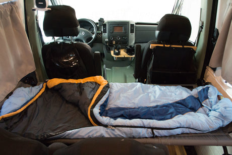RV rental camper interior: Bed with two sleeping bags, looking towards the driver's cabin and dashboard.
