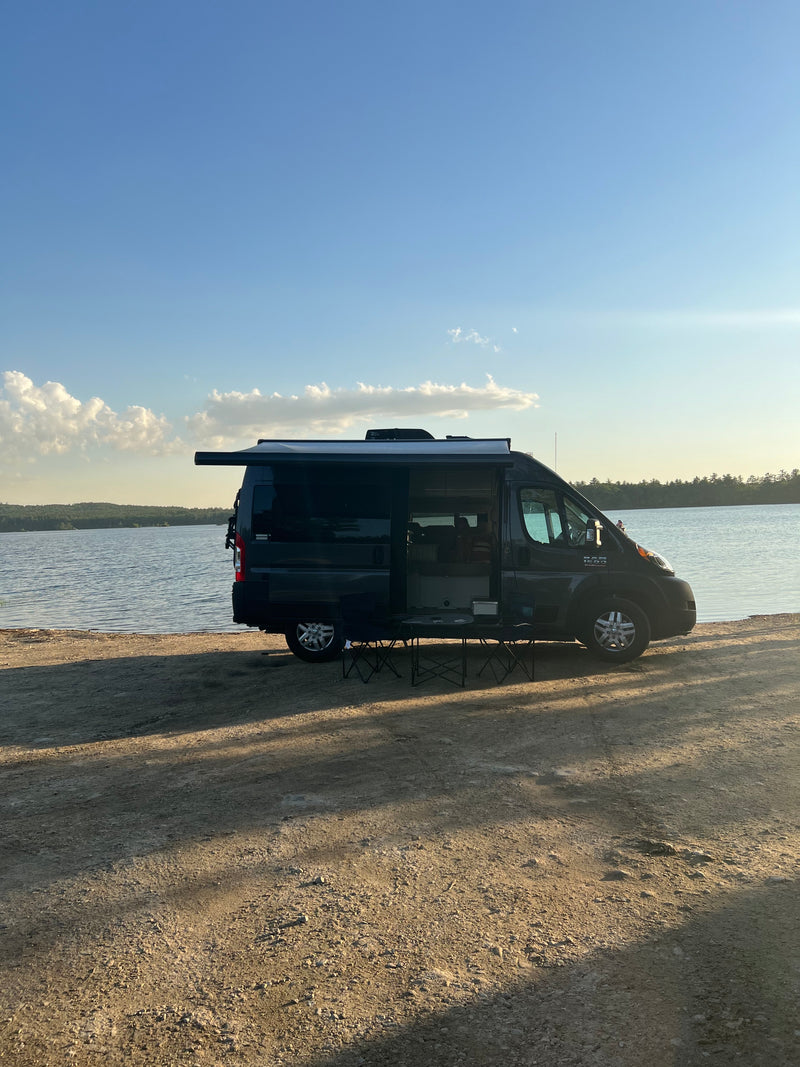 An RV rental, a dark camper van, parked lakeside with an extended awning & chairs for peaceful camping. — photo 2
