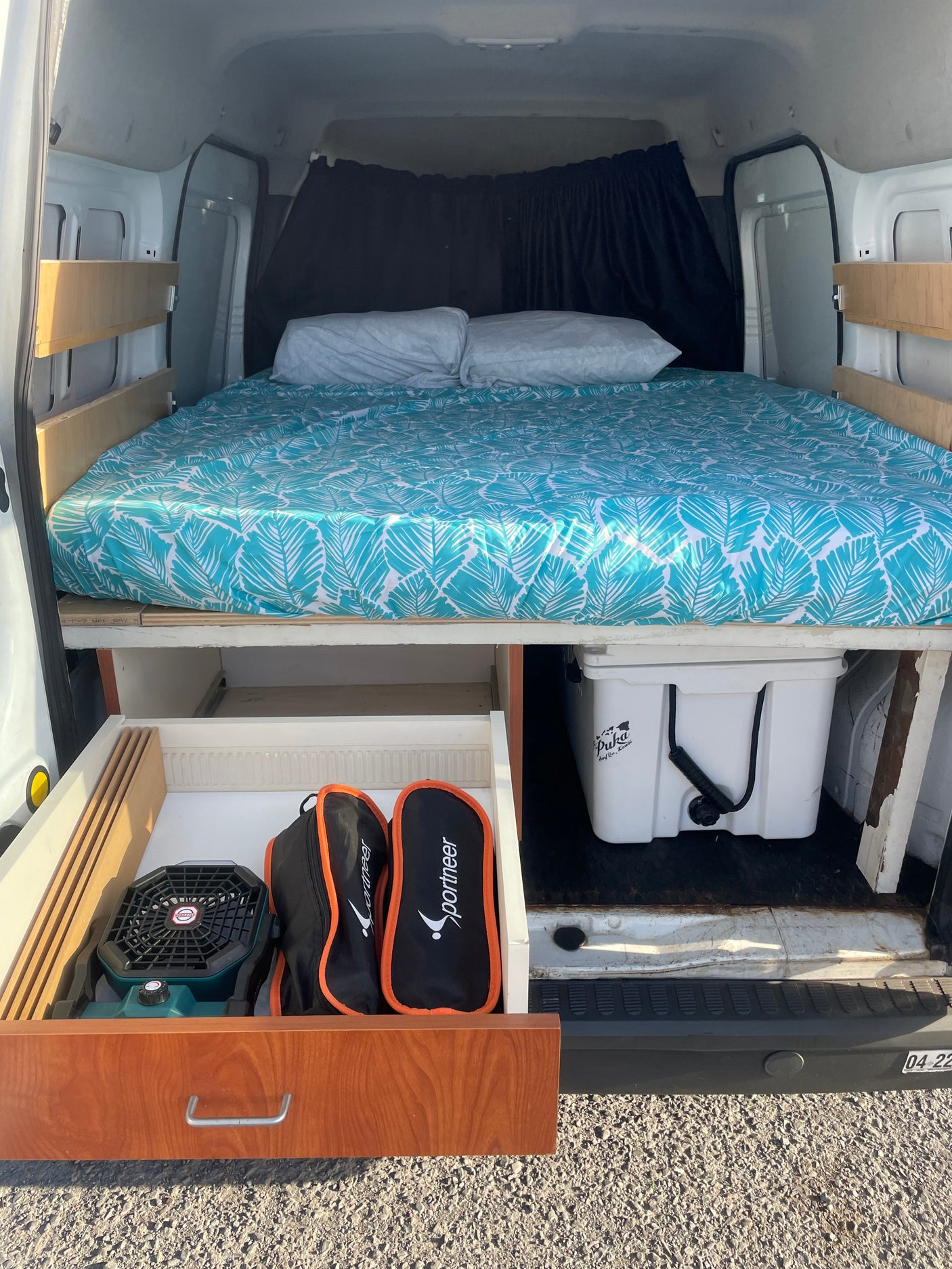RV rental van conversion: organized sleeping area with bed, pull-out storage, and cooler underneath. Ready for adventure.