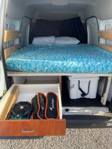 RV rental van conversion: organized sleeping area with bed, pull-out storage, and cooler underneath. Ready for adventure.