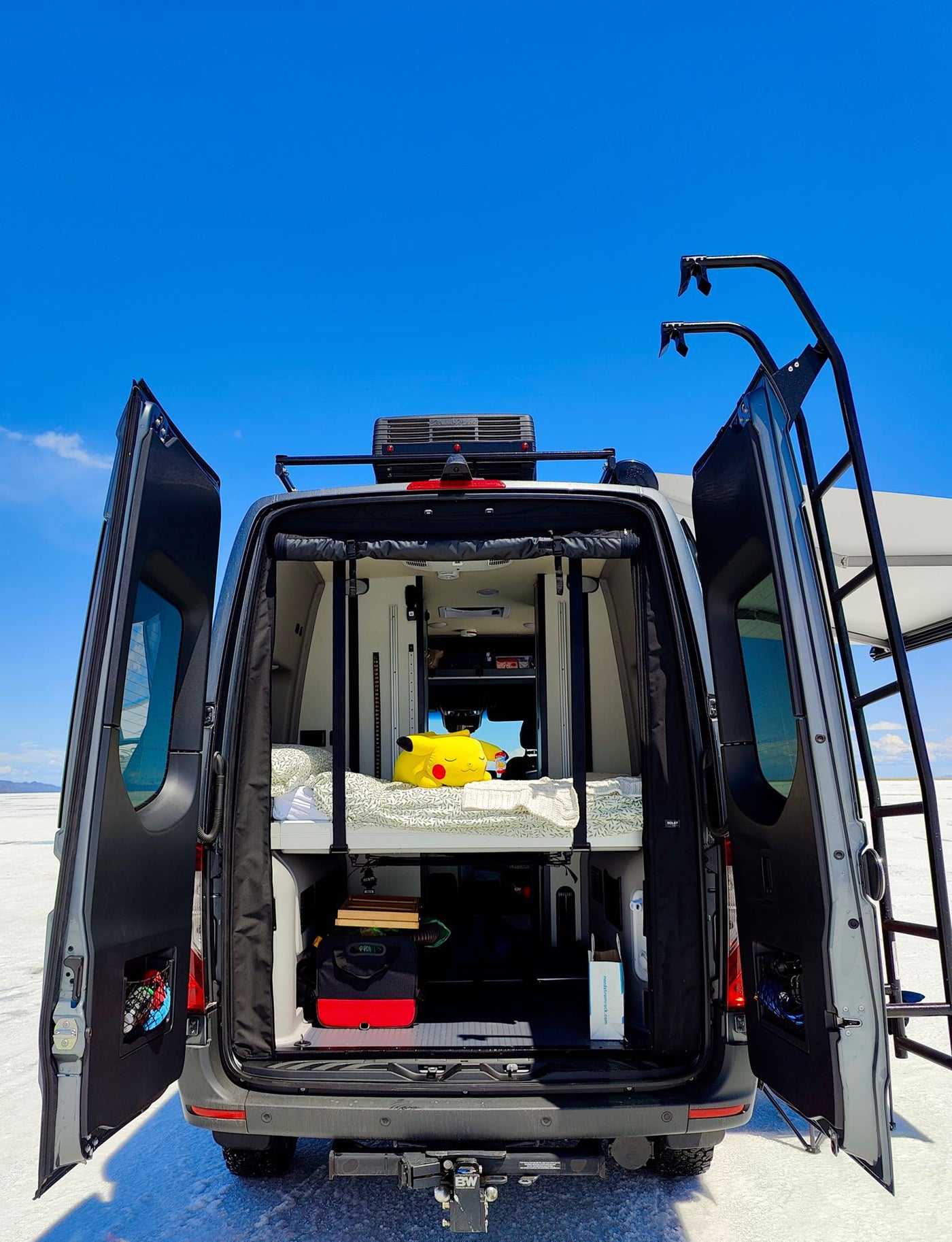 and sky. A Pikachu plush rests on the bed.|Relaxing RV rental setup: a grey Winnebago camper van with awning — photo 11