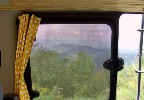 Enjoy nature's mountain views from your RV rental. A window screen reveals trees, framed by a yellow polka dot curtain.