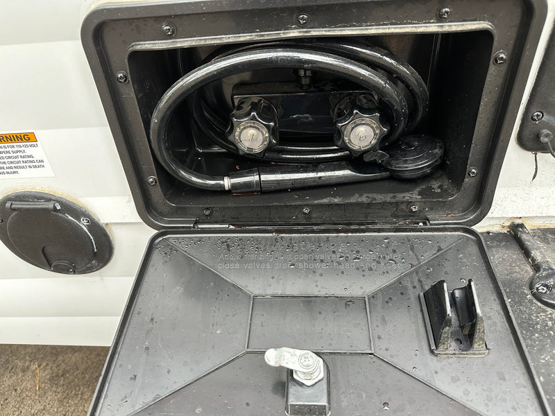 RV rental outdoor shower: An open exterior compartment shows the hose, hot/cold knobs, and winterizing instructions. — photo 10