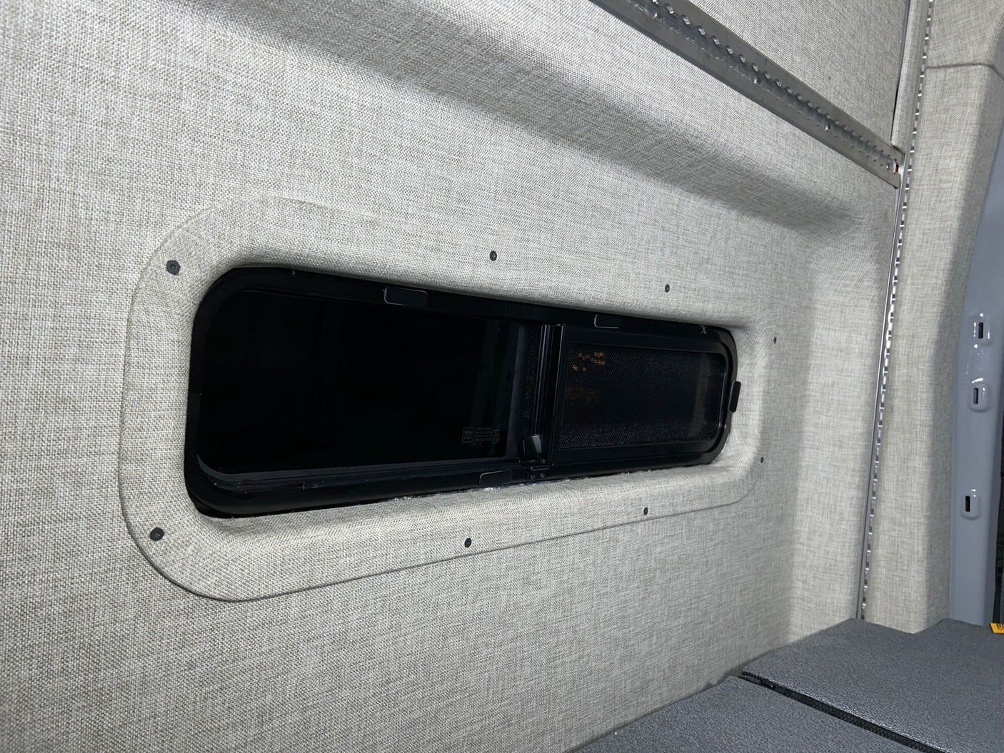 RV rental camper van interior featuring soft fabric walls, a modern window, and integrated L-track storage.