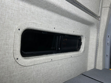 RV rental camper van interior featuring soft fabric walls, a modern window, and integrated L-track storage.