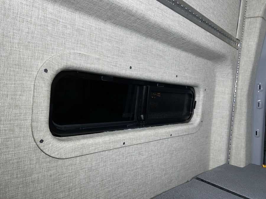 RV rental camper van interior featuring soft fabric walls, a modern window, and integrated L-track storage.