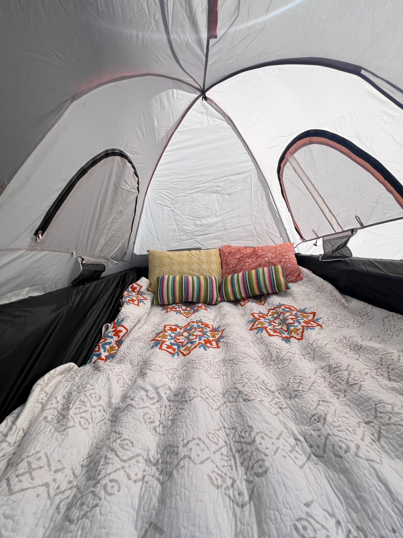 Comfortable glamping setup inside an RV rental. Features a cozy bed with a patterned quilt & colorful pillows.