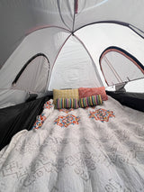 Comfortable glamping setup inside an RV rental. Features a cozy bed with a patterned quilt & colorful pillows.