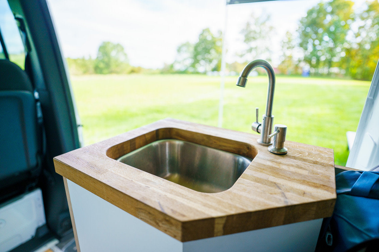 RV rental's compact kitchen with a built-in stainless steel sink, wood counter, and outdoor field view.