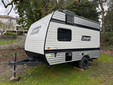 Small white and gray Coleman travel trailer parked on grass, ideal for your next RV rental adventure.