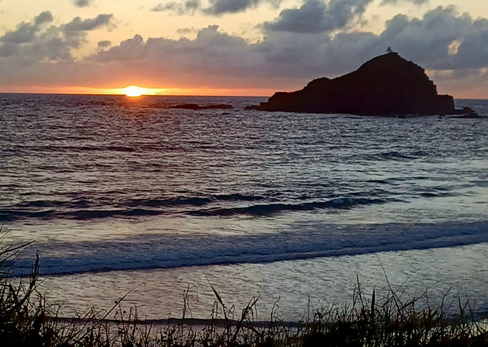 Sunset over a tranquil ocean with a silhouetted island. Plan your next RV rental escape!