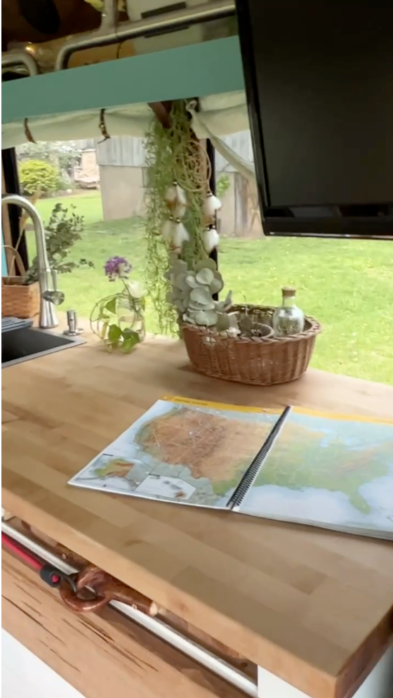 This RV rental's cozy kitchen features a sink, plants, and maps on a wooden counter, ideal for travel planning. — photo 6