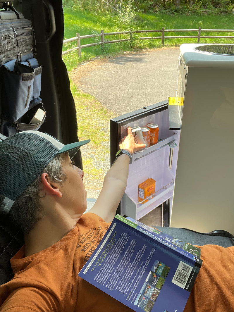Person in an RV rental, relaxing with a hiking guide and reaching for a cold drink from the mini-fridge. — photo 16
