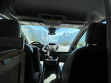 RV rental van interior showing dashboard, steering wheel, and seats, with a majestic mountain view outside. Ideal for travel.