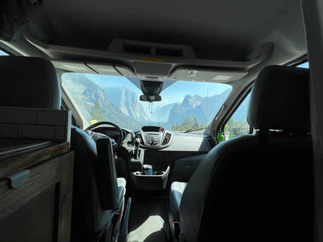 RV rental van interior showing dashboard, steering wheel, and seats, with a majestic mountain view outside. Ideal for travel.