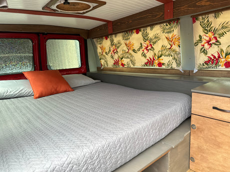 Cozy RV rental interior featuring a quilted bed, tropical-patterned curtains, and wood trim details.