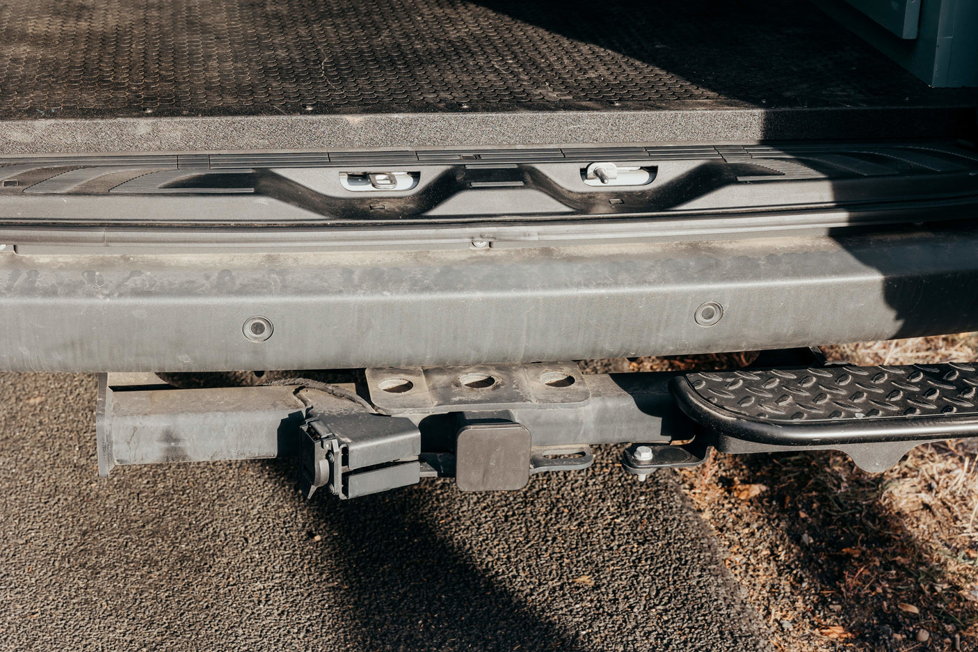 Rear view of an RV rental's bumper with a tow hitch, electrical hookup, parking sensors, and a step. Ready for adventures!