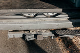 Rear view of an RV rental's bumper with a tow hitch, electrical hookup, parking sensors, and a step. Ready for adventures!