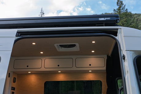 Spacious RV rental camper van interior with ceiling lights, overhead storage, and an exterior Fiamma awning visible.