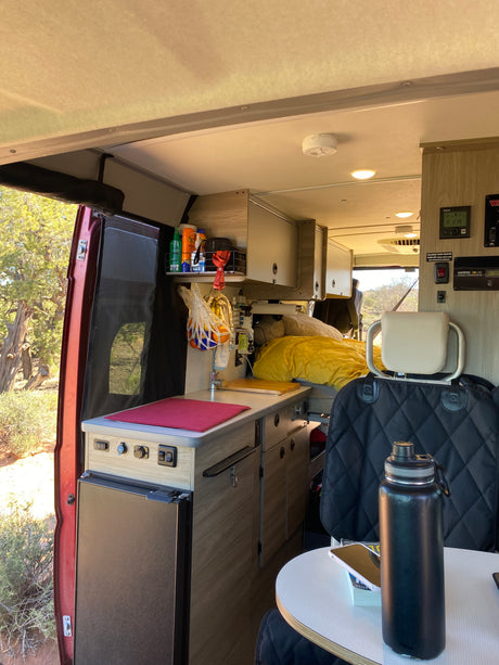 Interior of an rv rental showing a compact kitchen, bed, and desert landscape view outside. Ideal for travel.