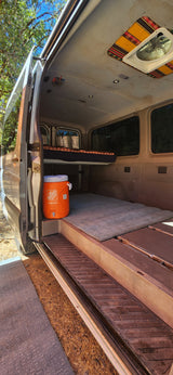 RV rental: Inside a converted van with elevated bed, cooler, and a colorful patterned roof vent.