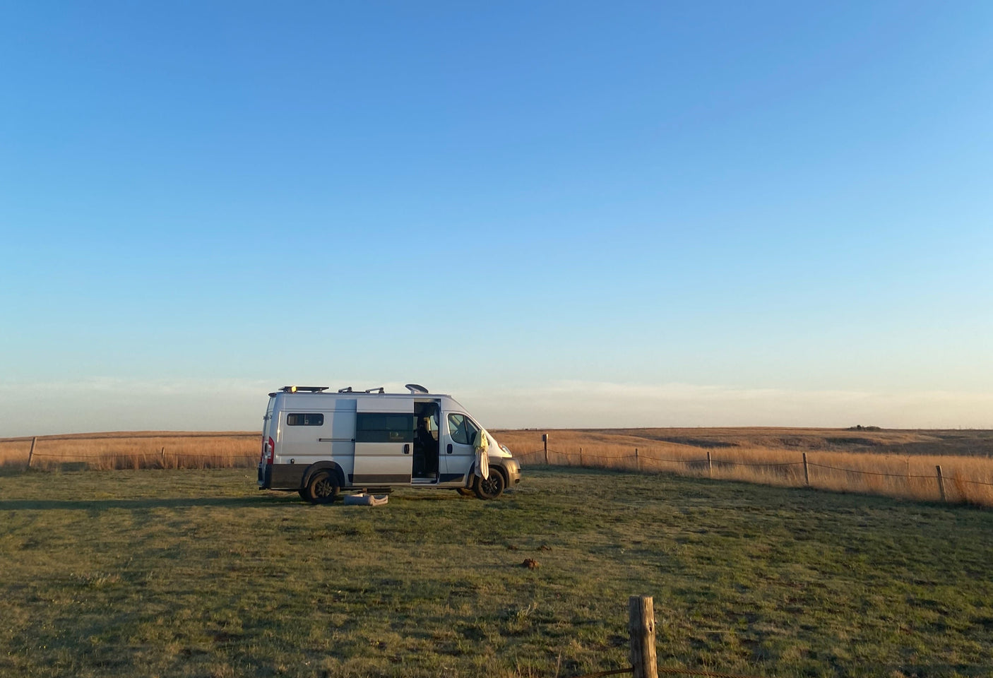 An rv rental camper van sits in a green field under a clear blue sky, with golden prairie extending to the horizon.