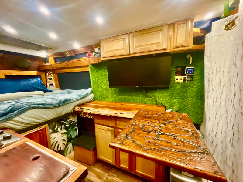 Inside a unique RV rental: bed, kitchen area, TV, and stunning custom wood countertops with a green wall accent. — photo 15