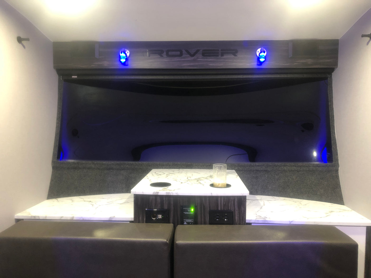 Modern RV rental interior features a compact dining area with a stylish table, comfortable seating, and blue ambient lighting.