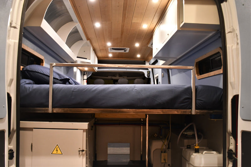 Interior of an RV rental: Elevated bed with blue bedding, wood ceiling, and under-bed storage for utilities. — photo 12