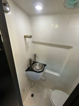 Compact RV rental wet bath: Features a toilet, small sink, shower, and towel bar within a molded white enclosure.