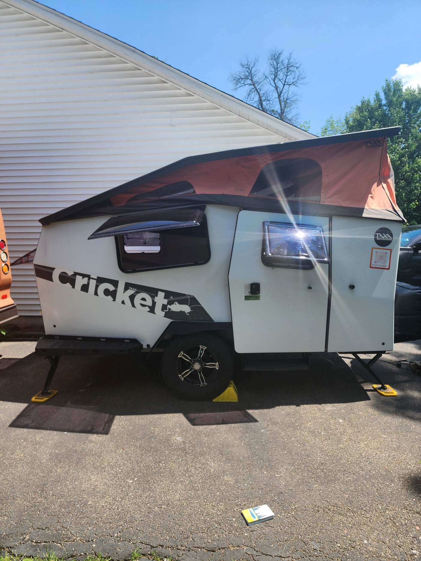 Compact Taxa Outdoors Cricket RV rental with pop-up roof, parked on pavement. A unique travel trailer for adventure.