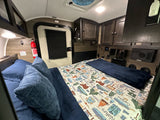 Cozy RV rental sleeping area featuring a nature-themed bed, exit door, fire extinguisher, and overhead storage.