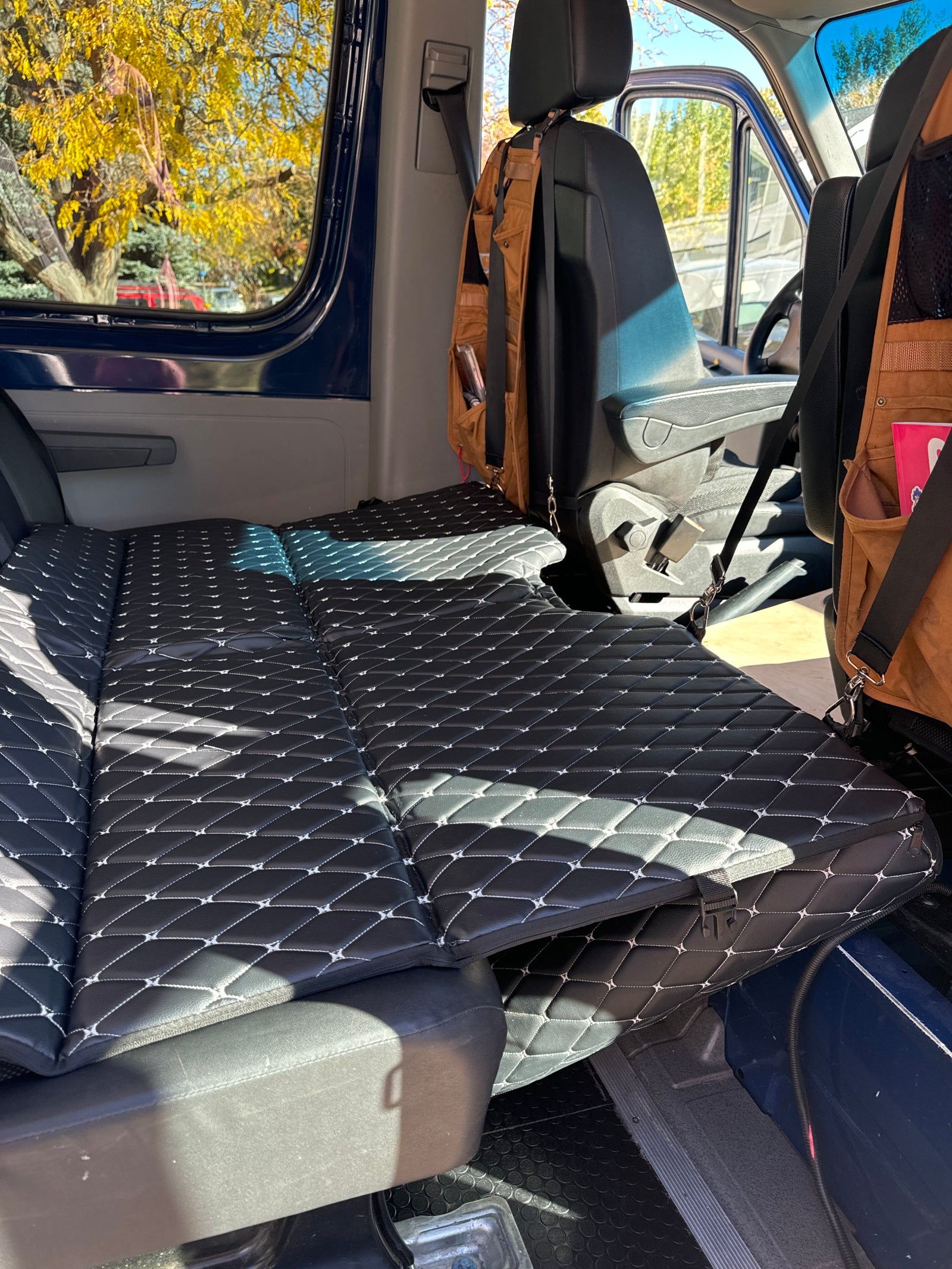 Black quilted mattress fills this RV rental van's interior, showing autumn leaves outside. Ready for adventure!
