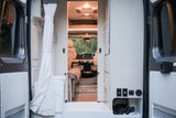 Experience comfortable rv rental adventures! View inside a camper van from open rear doors, showing the living area, bathroom, and front cab.