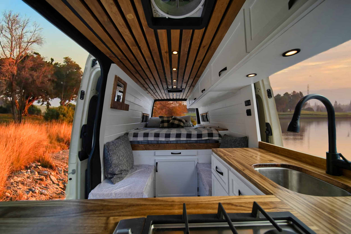 Modern rv rental interior features a slatted wood ceiling, built-in kitchen with sink & stovetop, a comfy bed, and nature views. — photo 2