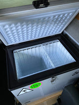 This open portable fridge/freezer, ideal for an rv rental, features two empty wire baskets & a 'Catch Surf' sticker.