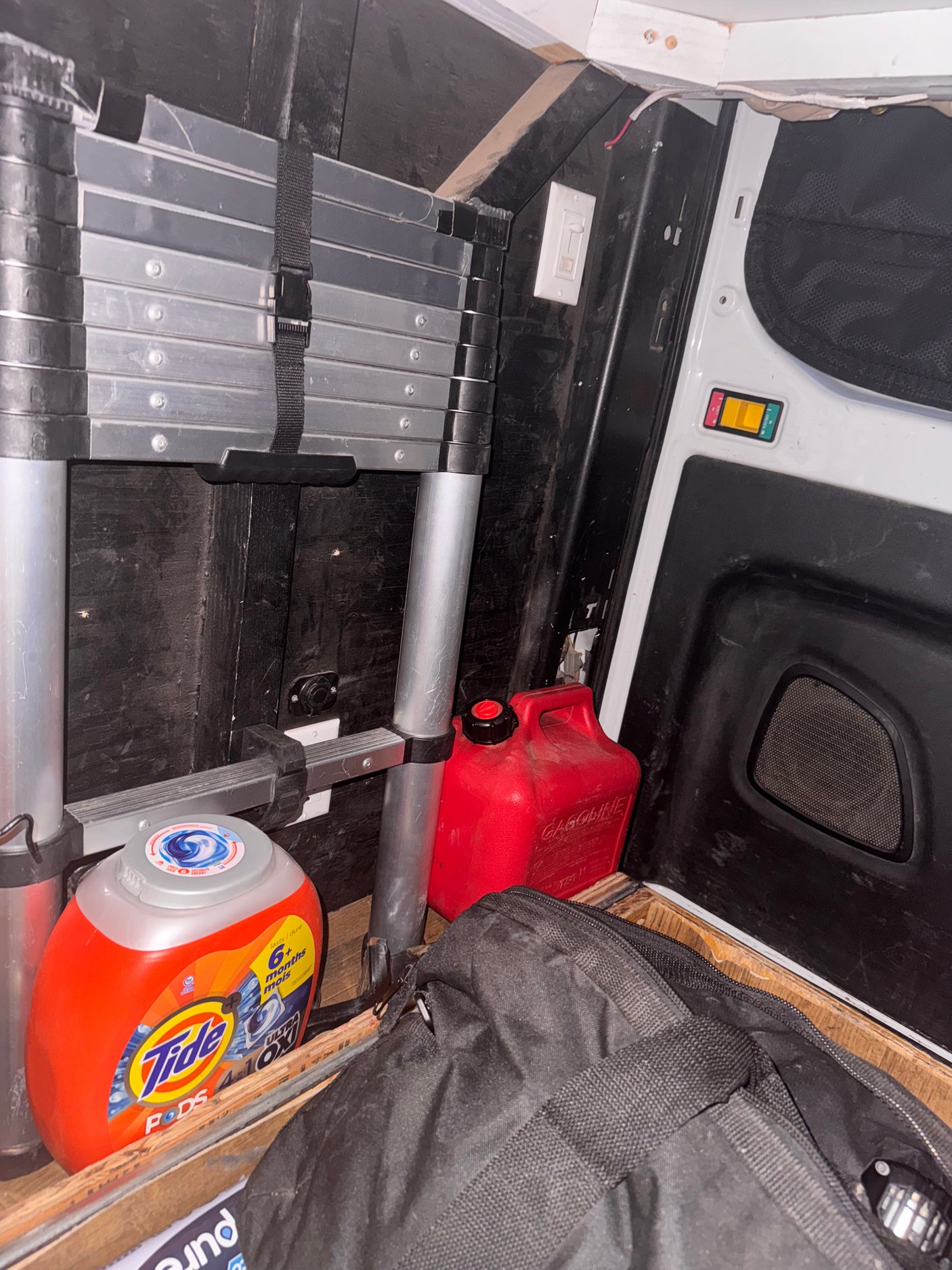 Stored essentials for your RV rental: a collapsible ladder, gas can, Tide Pods, and bag in the vehicle's cargo area.