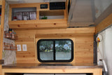 Inside a stylish rv rental: light wood paneling, counter, shelves, and a large window create a functional and cozy space.