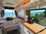 **RV rental** interior with a comfortable bed, modern cabinets, and a counter. Enjoy stunning ocean views from this cozy camper van.