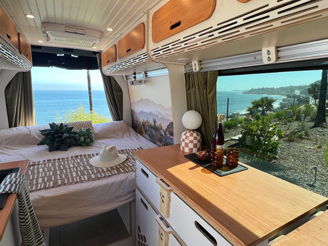 **RV rental** interior with a comfortable bed, modern cabinets, and a counter. Enjoy stunning ocean views from this cozy camper van.