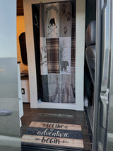 RV rental interior: A compact shower with adventure-themed curtain (bears, mountains) & 'Let the adventure begin' mat.