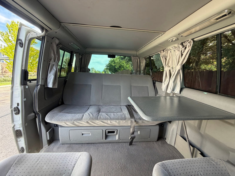 Inside this RV rental camper van, featuring a rear seat that converts to a bed, a foldable table, curtains, and storage. — photo 6