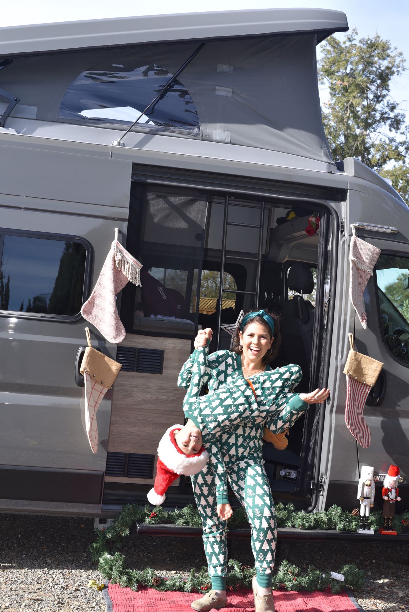 Festive family fun with an RV rental! A woman holds a child upside down in front of a decorated camper van.