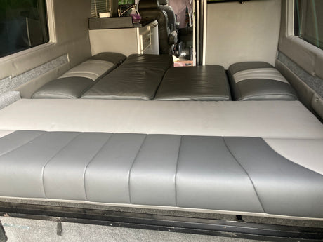 Spacious gray and white RV rental camper van interior. Features a convertible bed/seating setup and a compact kitchen.