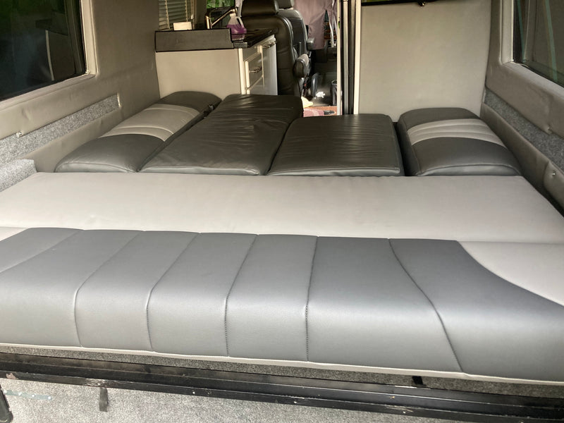 Spacious gray and white RV rental camper van interior. Features a convertible bed/seating setup and a compact kitchen. — photo 14