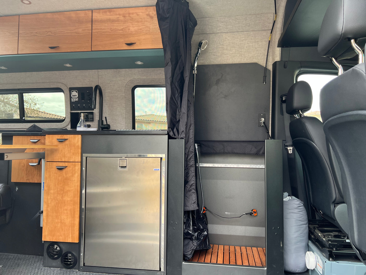 Explore this RV rental's compact interior: a full kitchen with wooden cabinets, fridge, and a clever shower area.